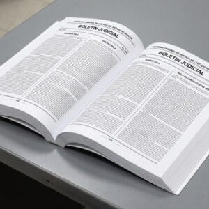 Ejemplar abierto del Boletín Judicial del Supremo Tribunal de Justicia del Estado de Sinaloa sobre un escritorio de melamina gris, con las dos planas impresas a dos columnas encabezadas por las salas.